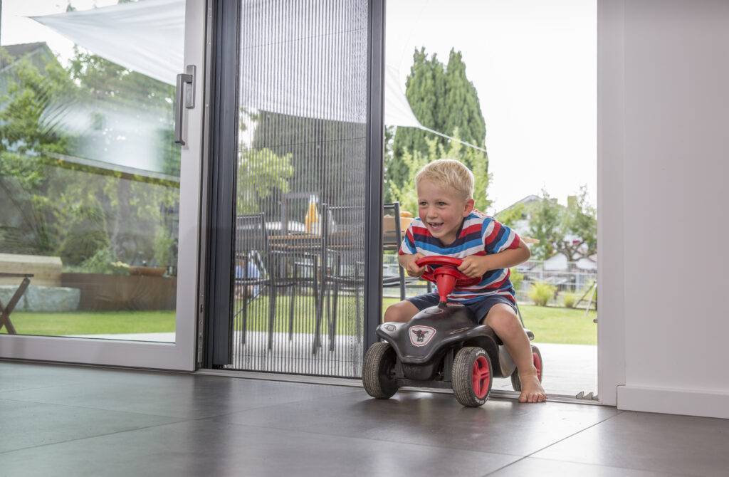 Child drives a bobby car over a threshold-free insect screen pleated blind