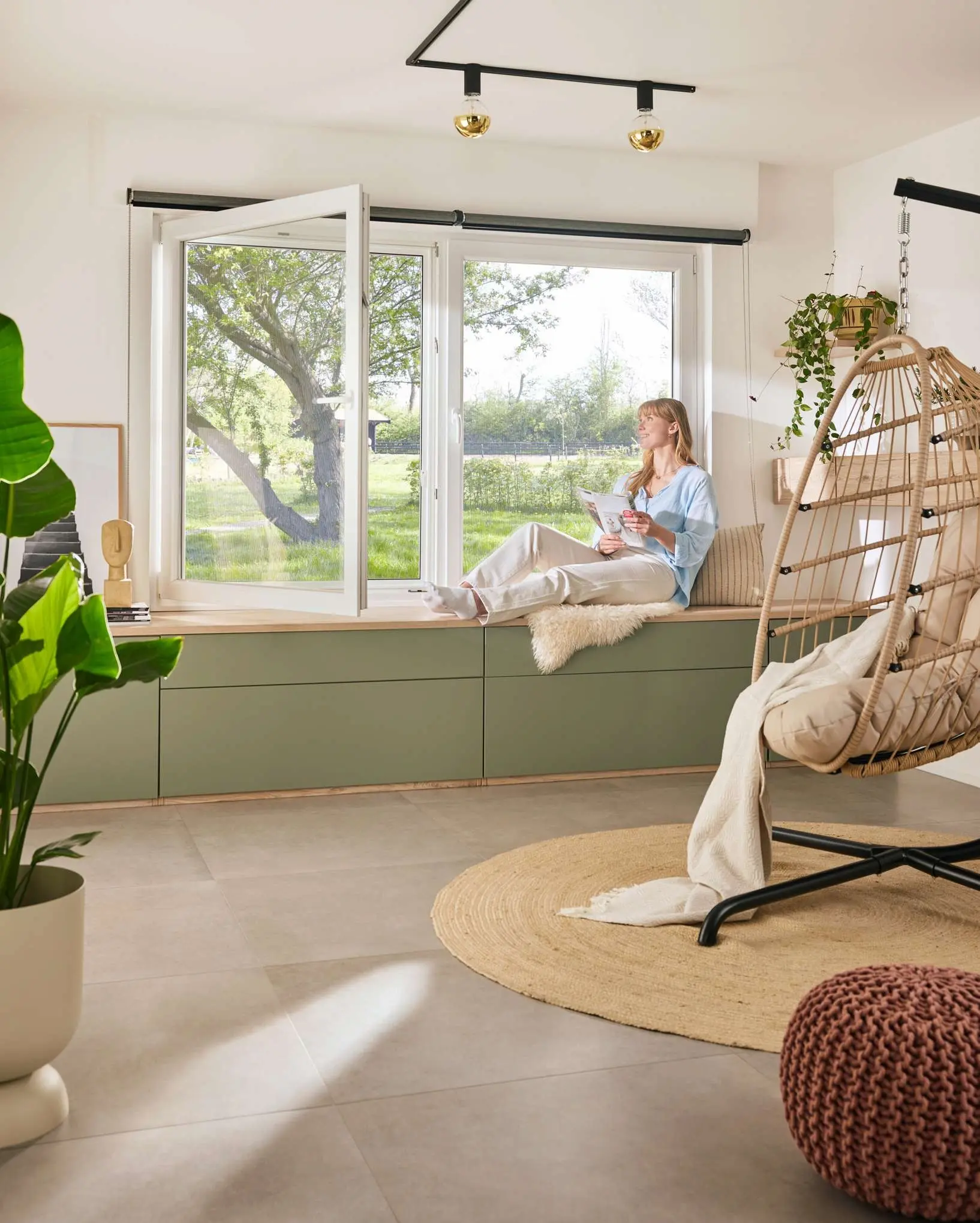 Helles Wohnzimmer mit grossem offenem Fenster, eingebautem Fenstersitz, Zimmerpflanzen und Hängesessel mit Blick in den grünen Garten.